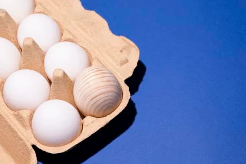 Paper packaging with white eggs and one wooden egg on a blue background Stock Photos