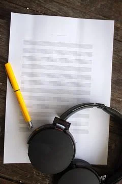 Paper sheet for musical notes with pen and headphone on wooden table. Stock Photos