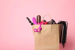 Paper shopping bag with different sex toys on red background, flat