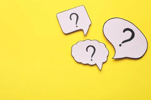 Paper speech bubbles with question marks on yellow background, flat lay. Sp.. Stock Photos