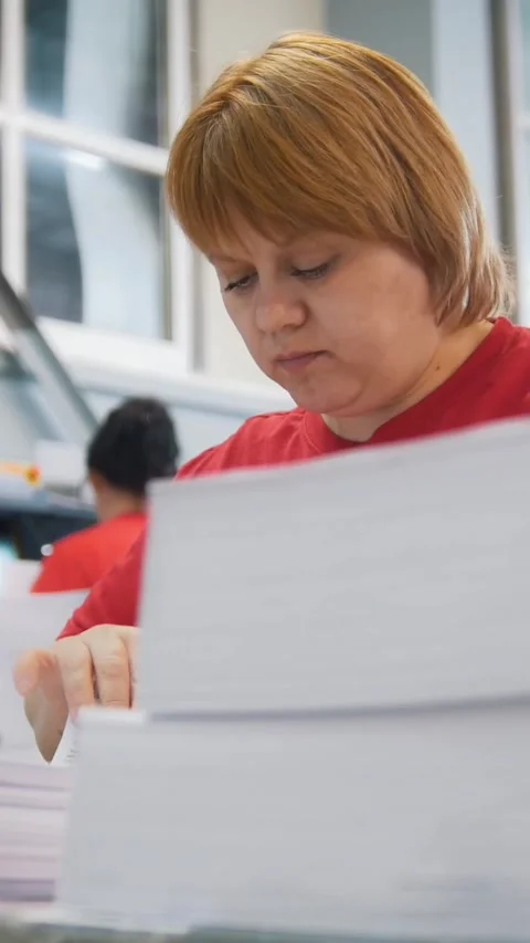Paper stack in front of woman worker sorting a printed edition in the typography Stock Footage 346706544
