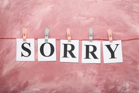 Papers with word SORRY hanging on string against pink grunge background Stock Photos