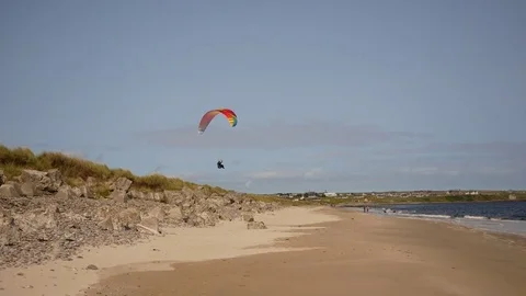 Para-glider flies close to low rocks at the beach Stock Footage 79628614