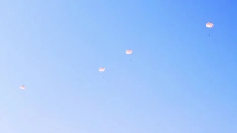 Parachutists float down with white parachutes against a clear blue sky. Video stock 286345491