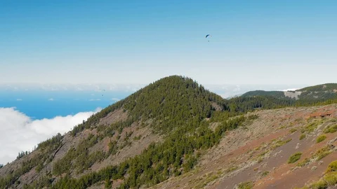 Paraglider above low dense clouds and mountain peak and green forest, Tenerife Stock Footage 120329740