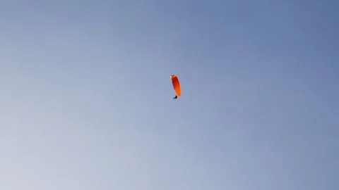 A Paraglider With a Bright Orange Canopy Soars Gracefully Through the Clear Sky Stock Footage 307576485
