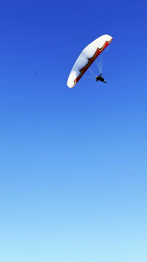 Paraglider in dynamic flight maneuvers set against a clear blue sky shot in Stock Footage 333604937