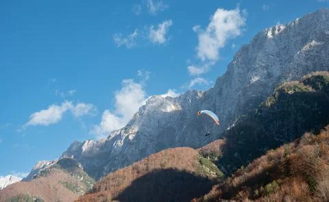 A paraglider elegantly glides through the sky, surrounded by towering mountain 스톡 사진