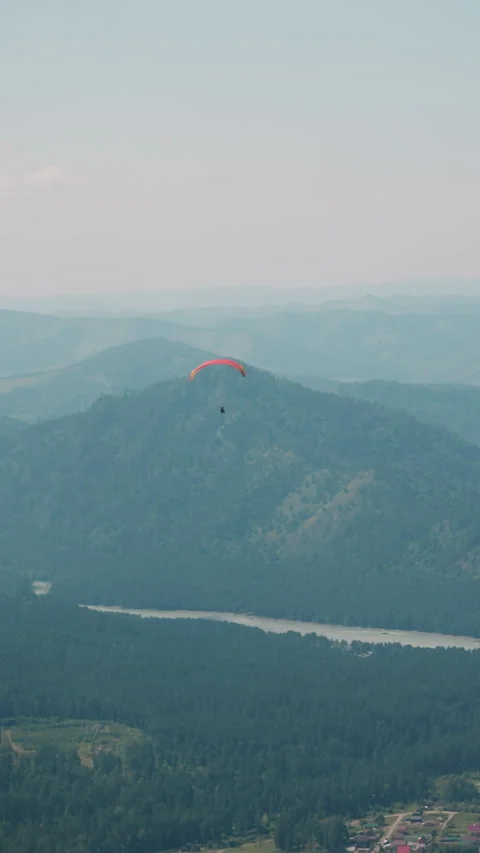 Paraglider flies over large green valley at mountains feet Stock Footage 290960304