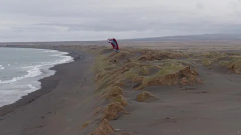 Paraglider flying above black sand dunes and coastal terrain in southwest Vidéo 344122921