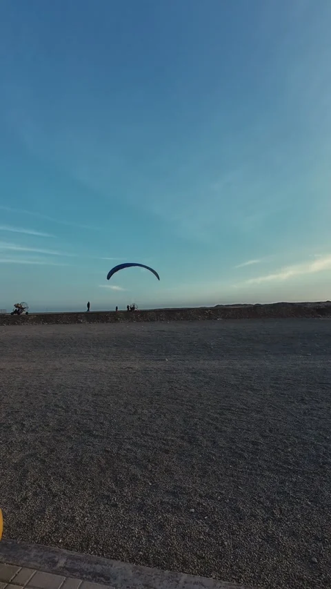 Paraglider flying over empty beach with yellow concrete ball in foreground Stock-Footage 307973107
