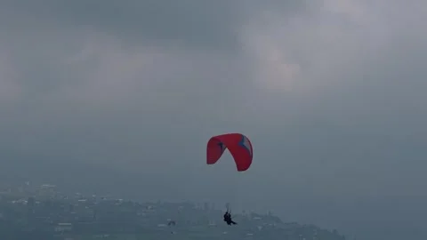 Paraglider flying with red canopy over misty hillside city, aerial adventure 動画素材 339122403