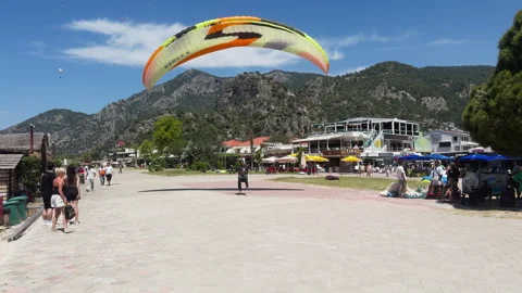Paraglider gracefully descends onto bustling seafront amonst tourists onlookers. Stock Footage 312444660