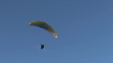 A paraglider gracefully glides through the azure sky, symbolizing the Stock Footage 274344379