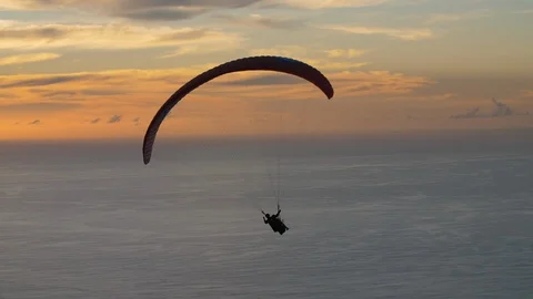 Paraglider makes a hard turn as he maneuvers the sky over ocean at dusk Stock Footage 101087287