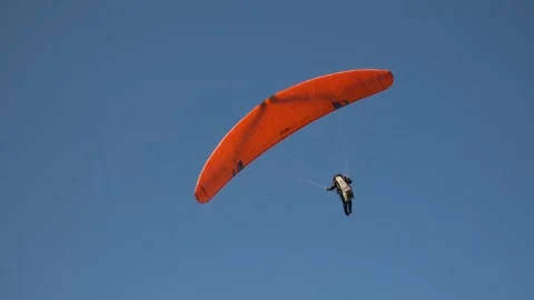 Paraglider with orange wing soaring against clear blue sky backdrop Stock-Footage 306489958