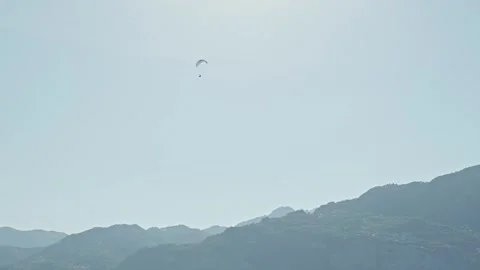 Paraglider pilot flying high above blue sunlight tinted mountains Stock Footage 313626613
