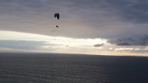 Paraglider sails by over the ocean on a cloudy late afternoon Stock Footage 81998860