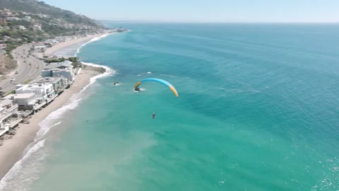Paraglider slow down for landing on sandy beach at oceanfront cottages in Malibu Video stock 217409089
