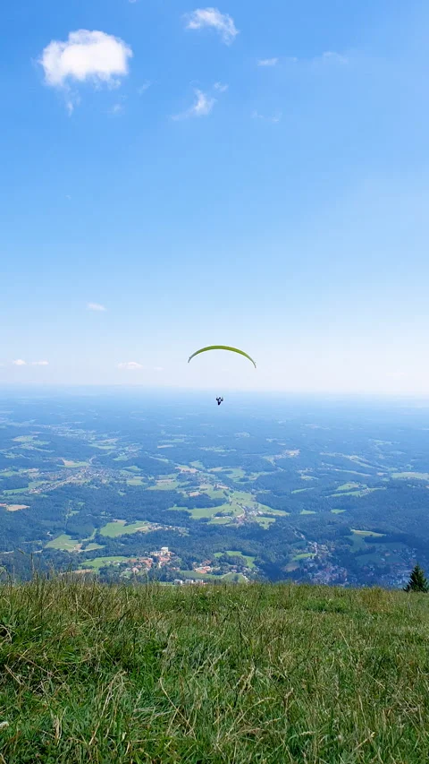 Paraglider Soaring Above Forest Under Blue Sky and White Clouds Over Mountains Stock Footage 331854029