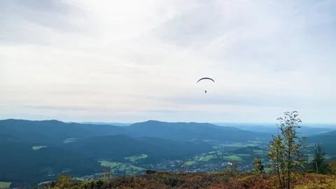Paraglider Soaring from a Mountain with Cloudy Sky and Stunning Forested Alpine  Stock Footage 294947997