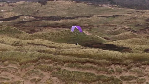 A paraglider soaring over grassy dunes in a peaceful and scenic outdoor Stock Footage 296794891