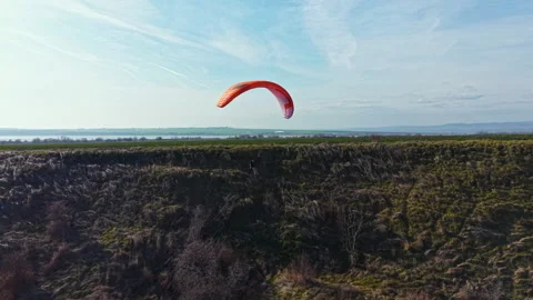 Paraglider soaring over a grassy hill near the water on a clear day with few Stock Footage 340156491
