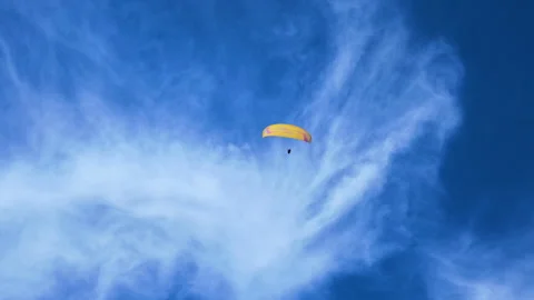 Paraglider soaring through a blue sky with swirling cirrus clouds in slow motion Vidéo 347943328