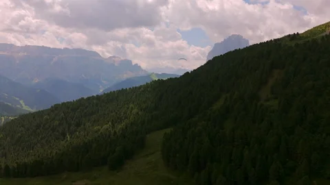 A paraglider soars above dense, forested slopes in the Dolomites, with Stock Footage 283546968