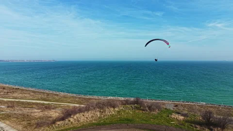 Paraglider soars above the ocean in a clear blue sky during daytime near the 스톡 동영상 336574406