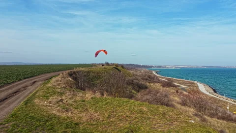 Paraglider soars over a coastal path near a grassy hill with clear skies and a Stock Footage 340155673
