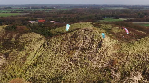 Paragliders doing some thrilling coastal soaring along vegetated Dutch dune 動画素材 325181804