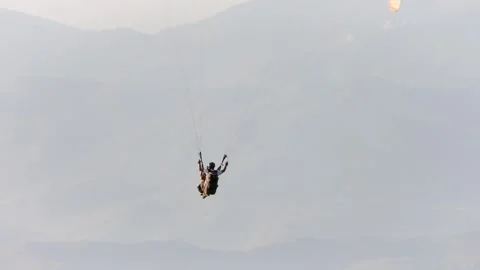 Paragliders fly above forested mountains and turquoise sea - Paragliding Flight Stock Footage 339934551