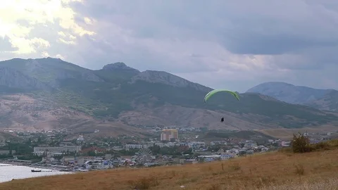 Paragliders fly against the backdrop of mountains and village Stock Footage 84549104