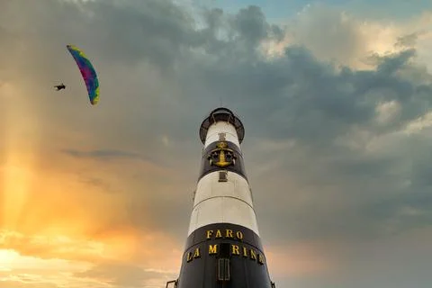 Paragliders fly next to the lighthouse at sunset on the coast of Lima, Peru Stock Photos