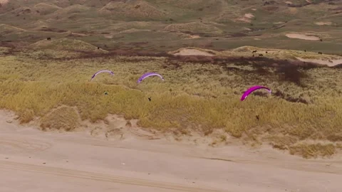 Paragliders fly by sand dunes in Castricum, Netherlands, wide drone shot Stock Footage 297673053