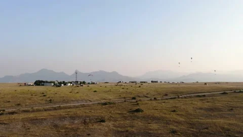 Paragliders hover over the hillside against the backdrop of a mountain range and Stock Footage 132191090