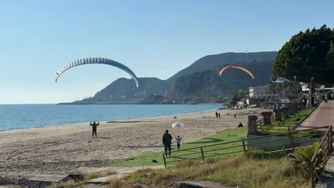 Paragliders soaring over a scenic beach with mountainous backdrop on a clea.. Stock Footage 336399055