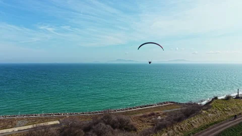 Paragliding above the ocean with a clear sky and distant hills visible in the Video stock 336519364