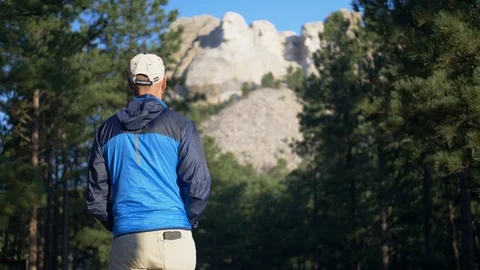 Parallax shot of man observing Mount Rushmore in forest and trees Video stock 102234953