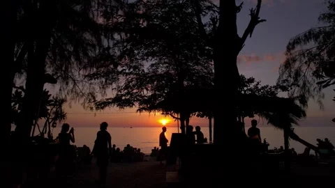 Parallel drone shot of gathering of people silhouetted against setting sun at Stock Footage 319607027