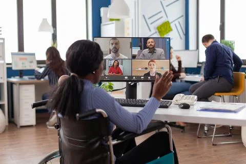 Paralyzed black worker sitting immobilized in wheelchair having videomeeting Stock Photos