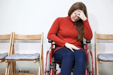 Paralyzed legs sad woman in invalid chair covers her face with hand while sit 스톡 사진