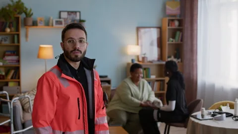 Paramedic Looking at Camera while Colleague Talking with Patient in Background Stock Footage 318898898