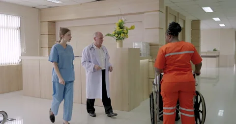 Paramedic in orange uniform assists elderly asian female patient in wheelchair Video stock 314001877