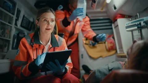 Paramedic Riding in Ambulance Using Tablet with Patient Stock Footage 141570351