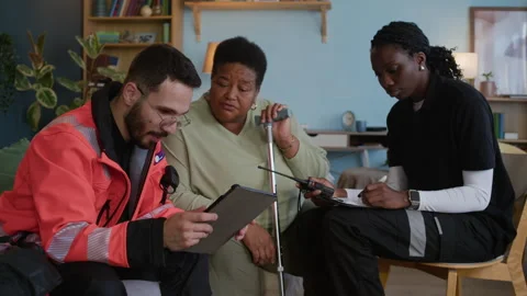 Paramedic Using Tablet Talking to Aged Woman while Colleague Assisting Stock Footage 318899730