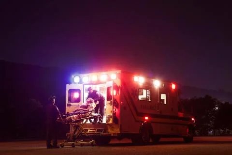 Paramedics carrying patient in ambulance at night Stock Photos