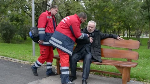 Paramedics rushing to help the old Man with a Heart Attack - Day in City Park Stock Footage 68743808