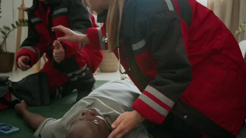 Paramedics Using Penlight to Assess Unconscious Patient Lying on Floor 스톡 동영상 293676162